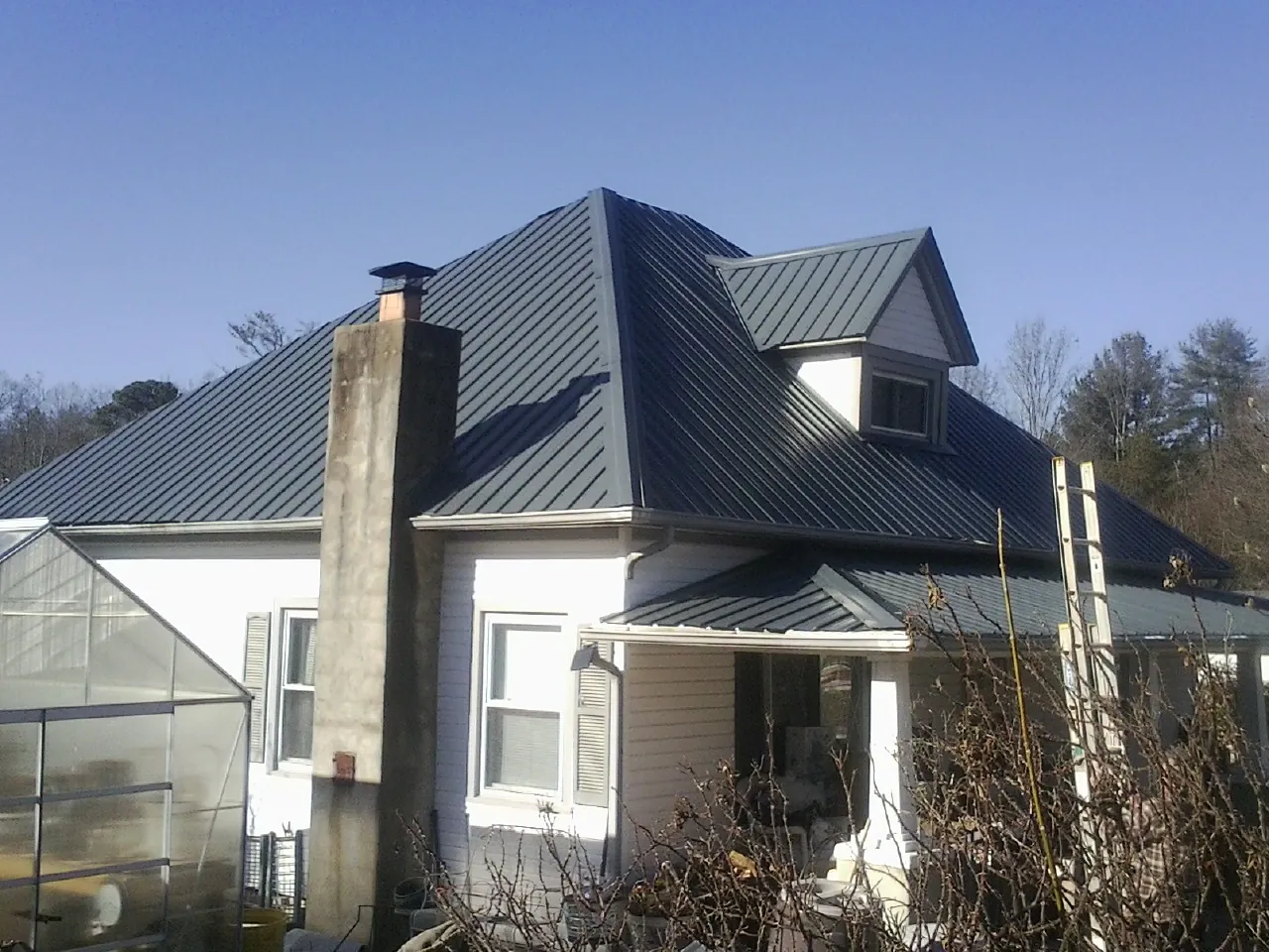 Dark blue standing seam metal roof on a white farmhouse with dormer — Slate & Tile Roof Repair by Roofing Brothers in Parker City