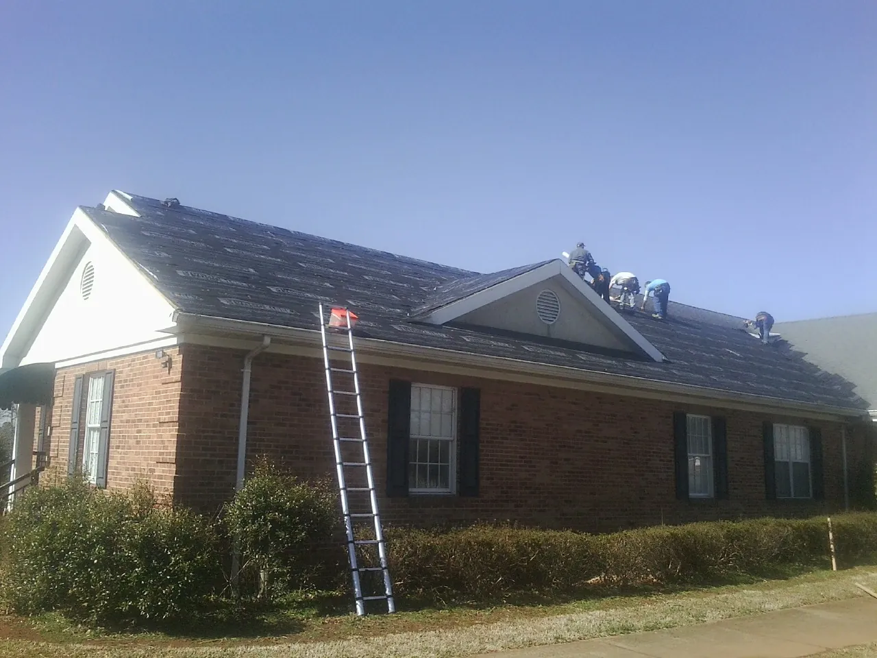 Crew tearing shingles off a brick ranch roof with a ladder set — Emergency Roof Repair work by our crew in Parker City