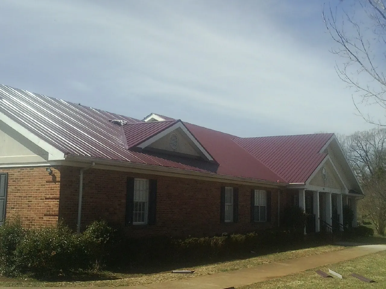 Red metal roof with gabled entries on a long brick building, from a Hail Damage Roof Repair job in Parker City