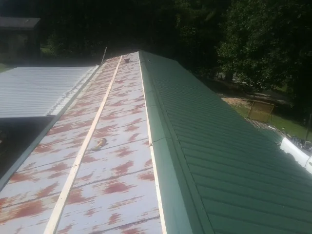 Old rusted panels beside newly installed green metal roofing — Wind Damage Roof Repair by Roofing Brothers in Parker City
