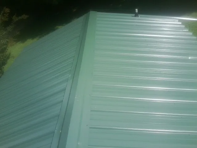New green metal panels meeting at the ridge of a roof — Flat Roof Repair work by our crew in Parker City