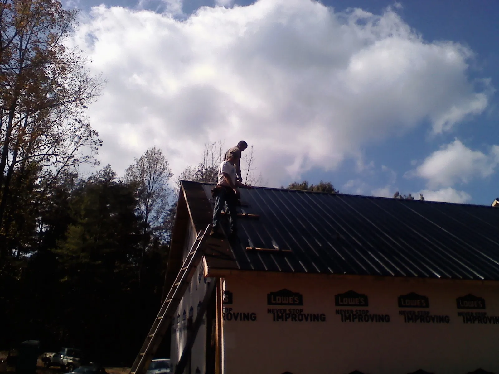 Roofer fastening dark metal panels high against a cloudy sky, from a Roof Inspection job in Parker City