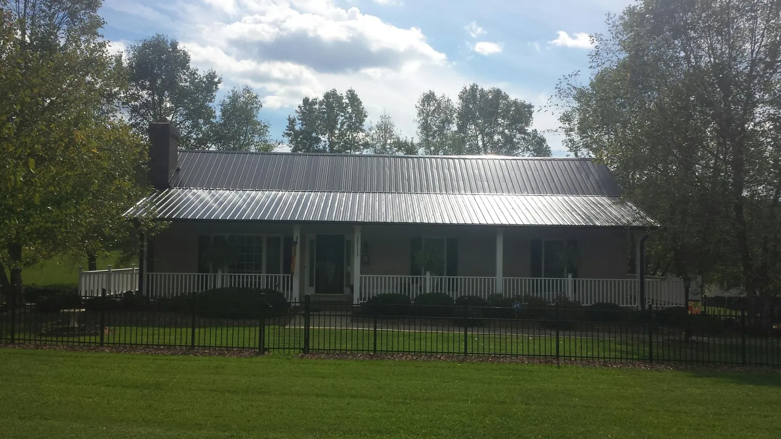 Gray metal roof on a brick ranch with a full width front porch — Gutter Guard Installation work by our crew in Parker City