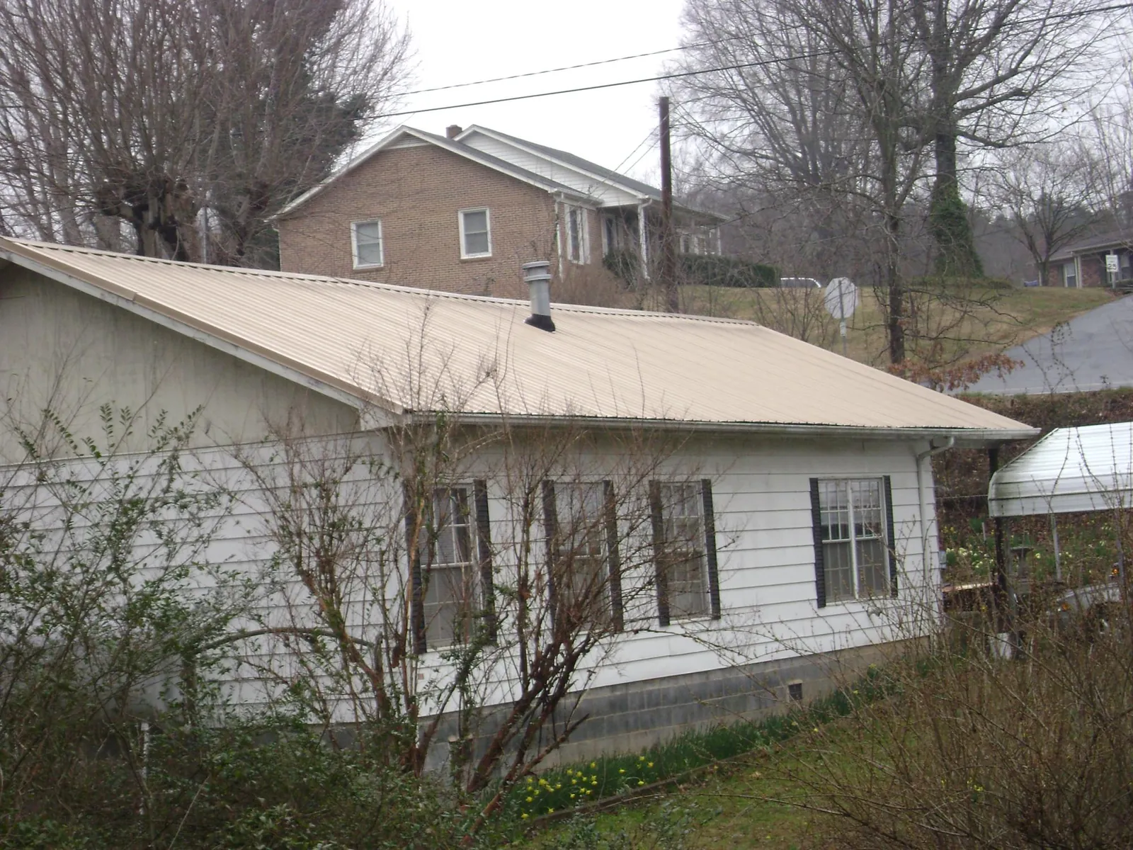 Tan metal roof on a white sided house set into a hillside — Commercial Roofing by Roofing Brothers in Parker City